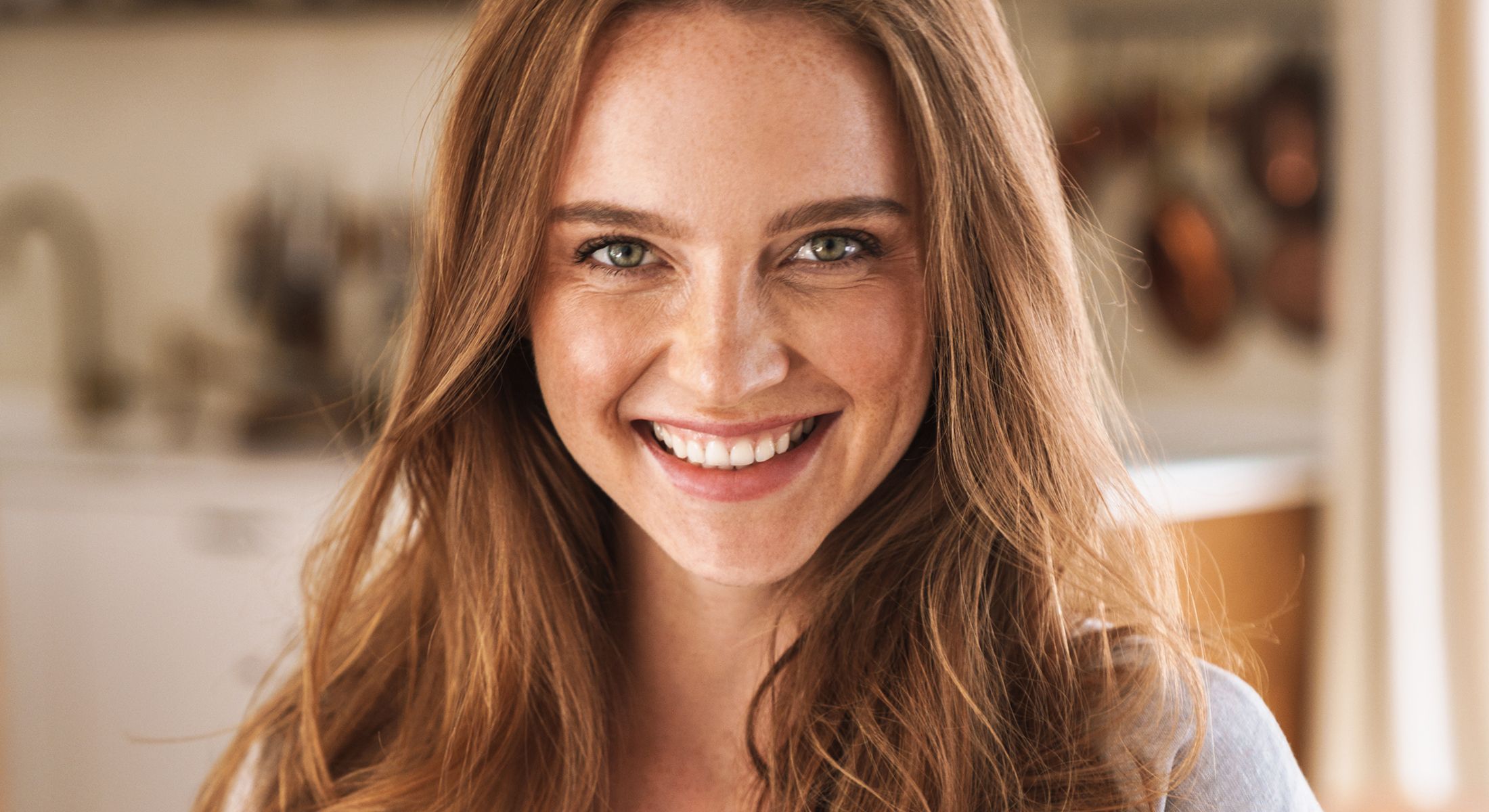 Smiling woman with long, wavy hair in kitchen.