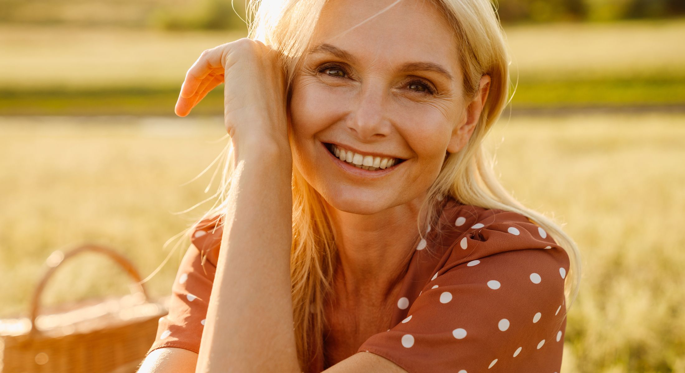 Smiling woman in a sunlit field setting.