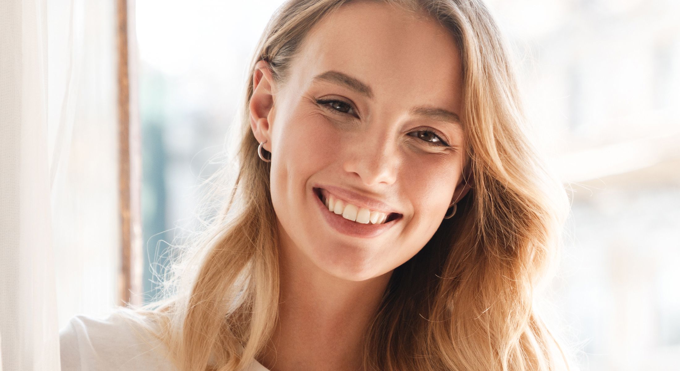 Smiling woman with long, wavy hair indoors.