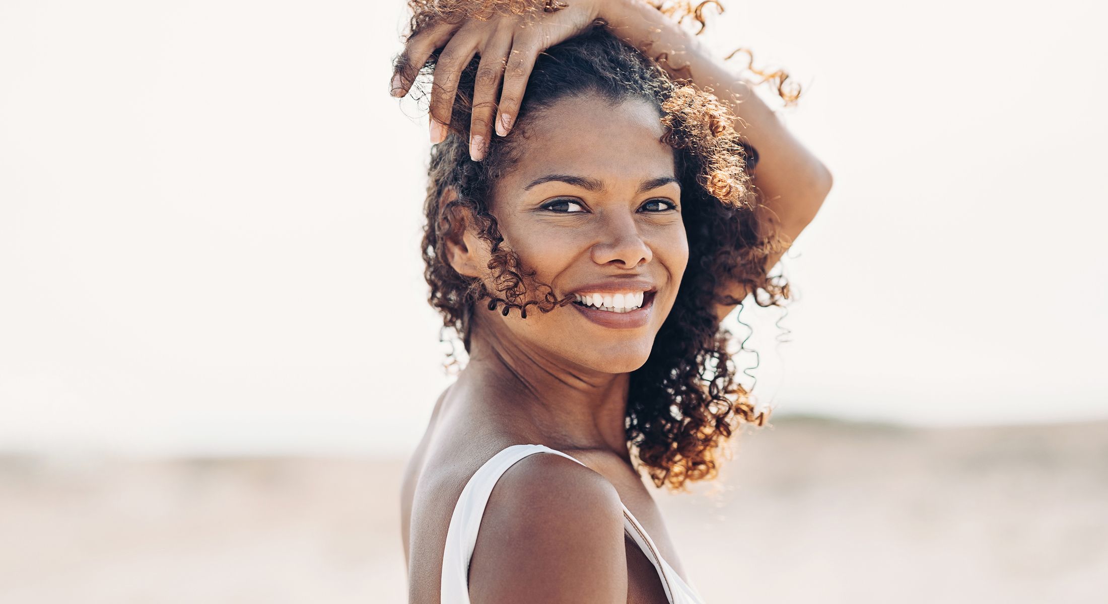 Smiling woman with curly hair at the beach.