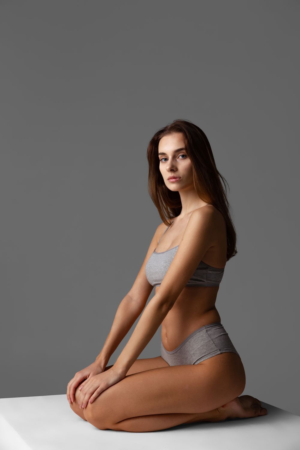 Model sitting, wearing gray lingerie, neutral background.