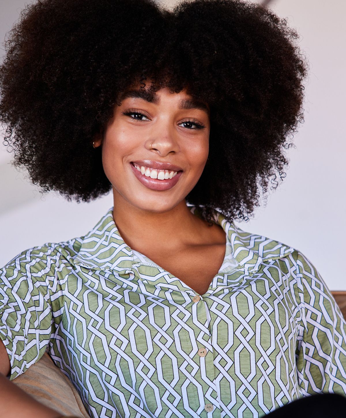 Smiling woman with curly hair in patterned shirt.