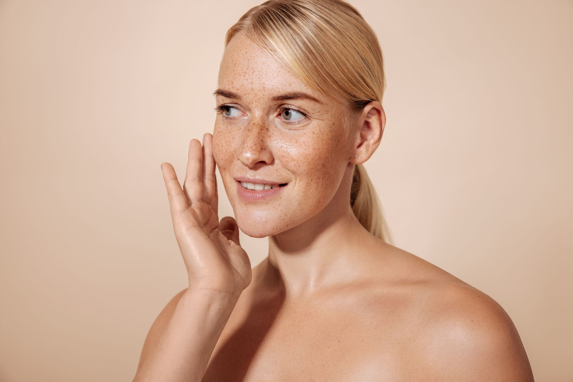 Woman with freckles smiling and touching her face.