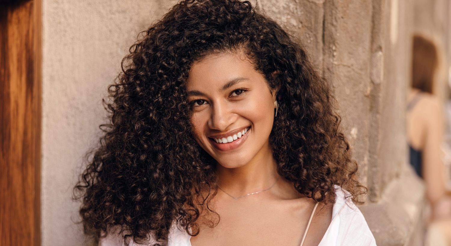 Smiling woman with curly hair against wall.