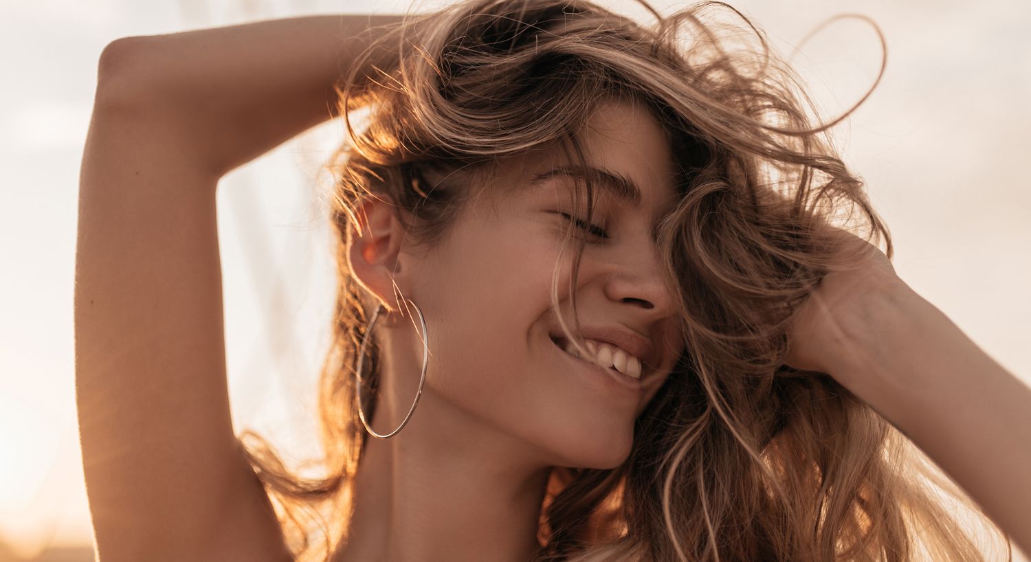 Smiling woman with flowing hair at sunset.