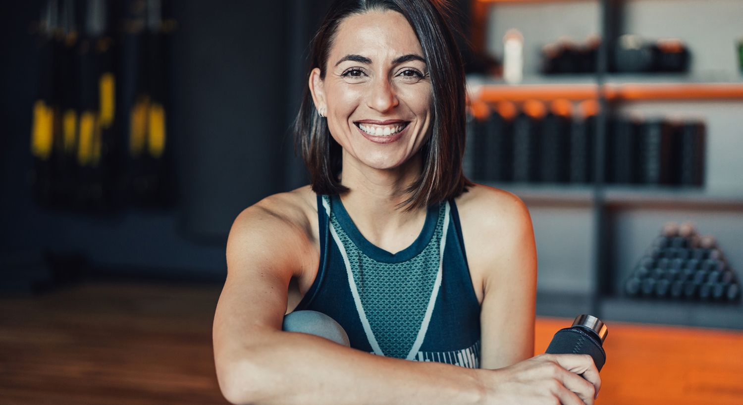 Smiling woman in fitness attire, holding water bottle.